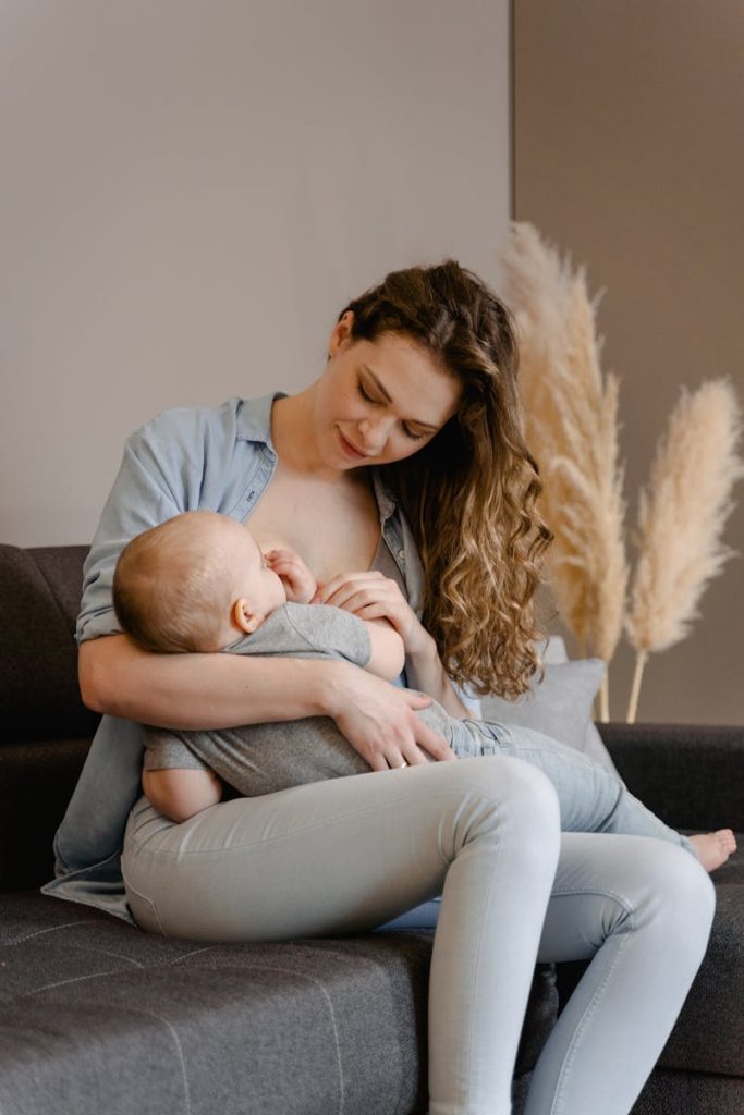 A tender moment of a mother breastfeeding her infant while seated on a sofa indoors.